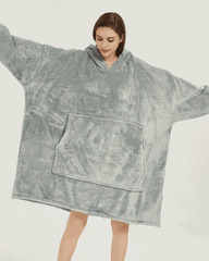 Light grey SNUGLFIT™ Hoodie Blanket worn by woman, showcasing oversized design and front pocket.