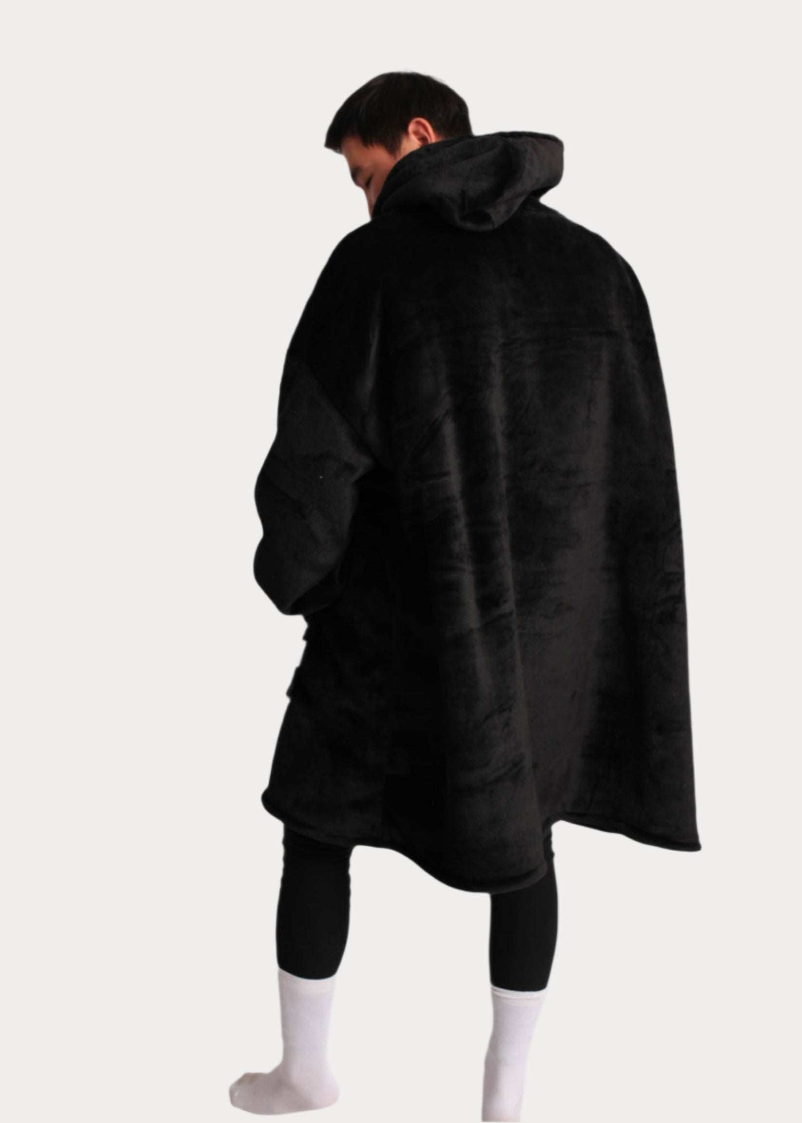 Oversized SnuglFit™ hoodie blanket in midnight black worn by a person, showcasing its plush, cozy design.