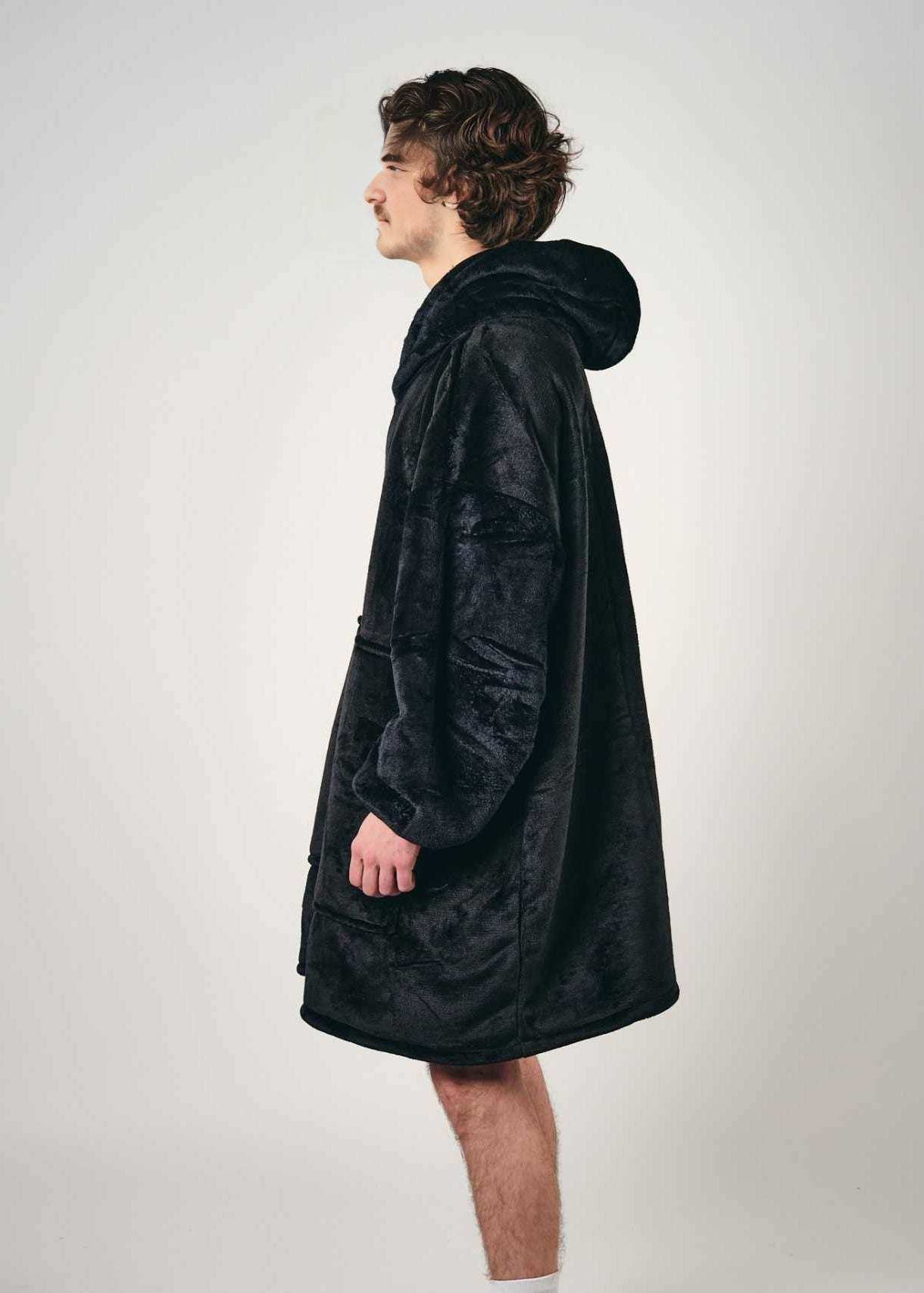 Man wearing SNUGLFIT™ Hoodie Blanket in Midnight Black, showcasing its oversized and comfortable design.