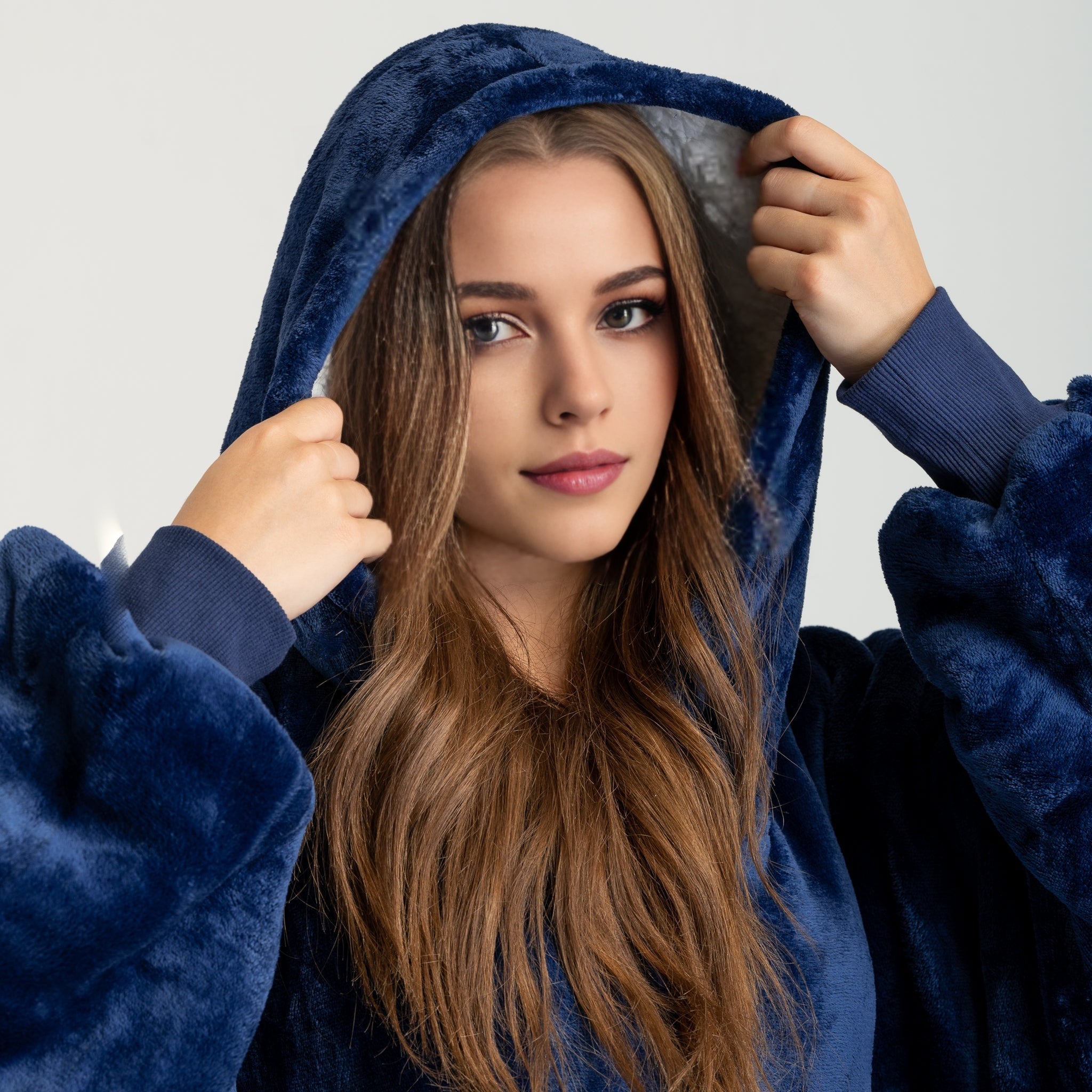 Navy blue SNUGLFIT™ Hoodie Blanket with plush Sherpa fleece interior, worn by a woman pulling up the hood for warmth and comfort.